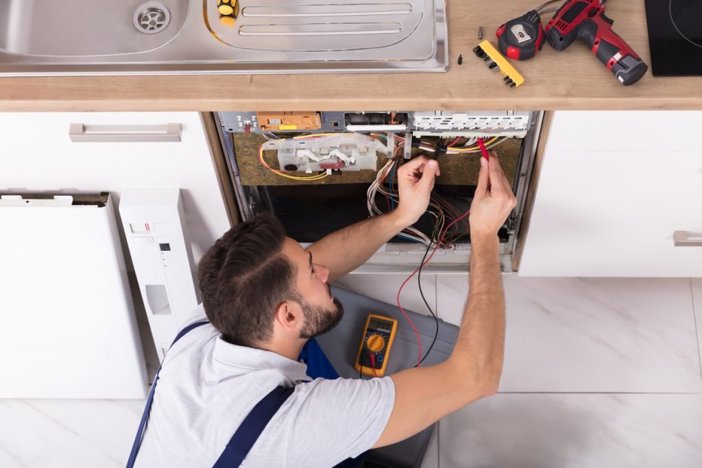 Male Technician in white shirt rewiring Dishwasher